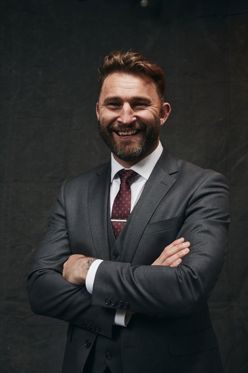 Professional photo of Paul Wood - Half Body professional image with black curtain and arms folded. Paul is wearing a smart suit and a red tie